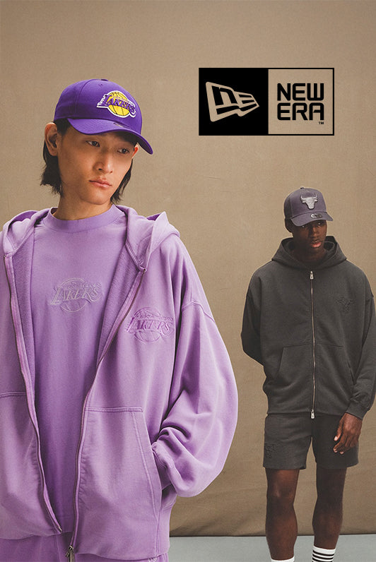 Two models wearing New Era sportswear and caps representing NBA teams, standing against a neutral beige backdrop with the New Era logo above.